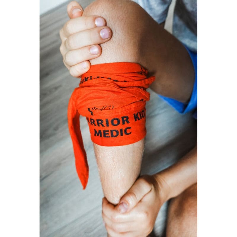 Person wearing orange 'Warrior Kid Medic' bandages on a leg with hands holding it.