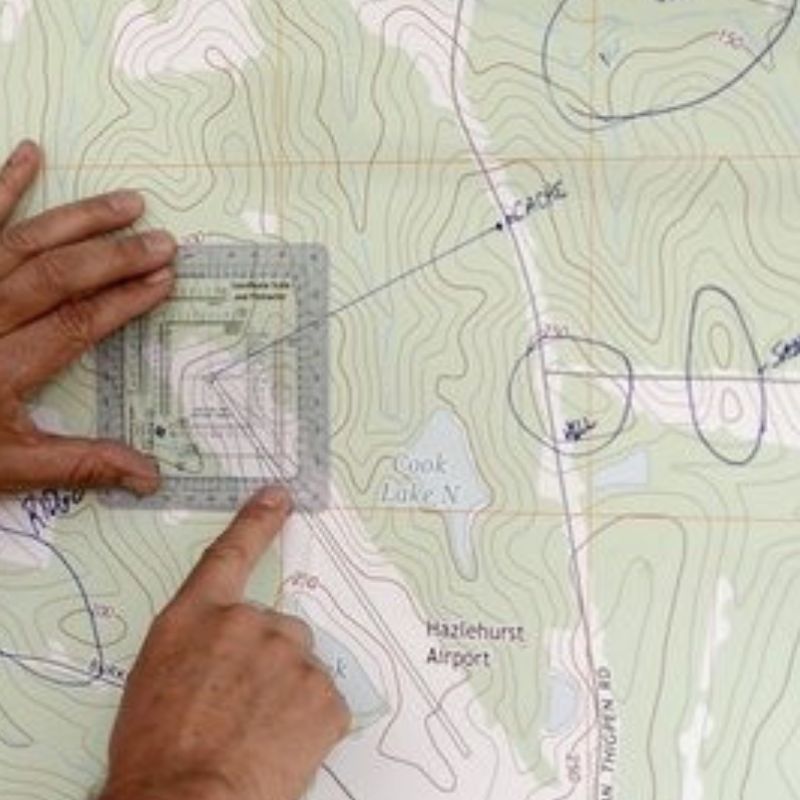 Land Navigation DVD or USB showing hands reading topographic map with compass, featuring custom kit builds A Way Through the Wilderness