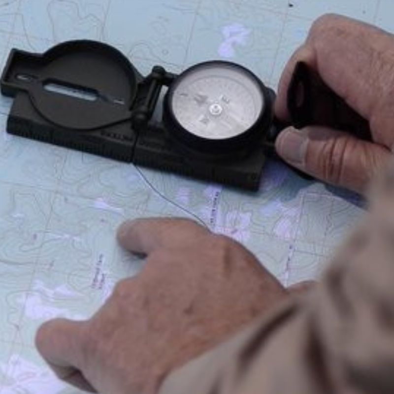 Land Navigation DVD or USB showing hands using compass on topographic map with custom kit builds A Way Through the Wilderness